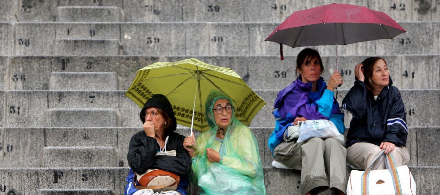 Gente protegiéndose de la lluvia con paraguas y chubasqueros Gente protegiéndose de la lluvia con paraguas y chubasqueros