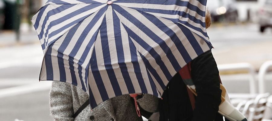 Dos mujeres se protegen con un paragüas de la lluvia y el viento en Pamplona Dos mujeres se protegen con un paragüas de la lluvia y el viento en Pamplona