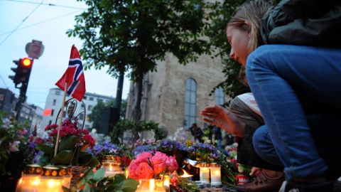 Una ni&ntilde;a coloca flores junto a banderas noruegas