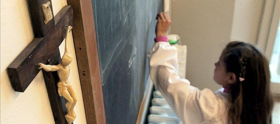 Una alumna escribe en la pizarra de una clase en la que cuelga un crucifijo Una alumna escribe en la pizarra de una clase en la que cuelga un crucifijo