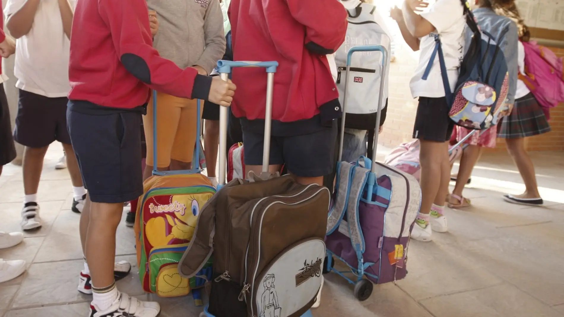 Varios niños llegan con sus mochilas al colegio. 