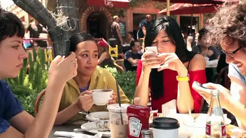 Tres personas consultan su teléfono móvil durante una comida Tres personas consultan su teléfono móvil durante una comida