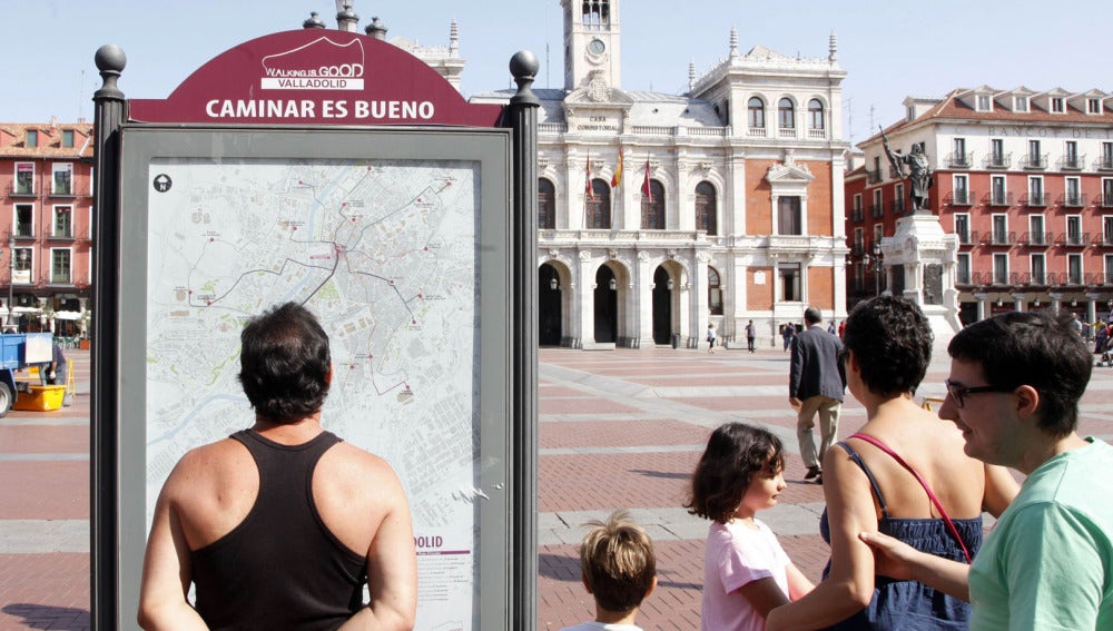 Una familia de turistas observa el panel informativo de las rutas 'Caminar es bueno' en la Plaza Mayor de Valladolid