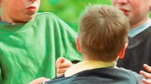 Representación de una escena de acoso escolar unos niños agreden a otro en el patio del colegio