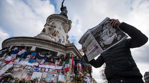 Un hombre lee la revista Charlie Hebdo frente al homenaje a las v&iacute;ctimas