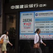 Dos mujeres pasan junto a una pantalla que muestra el índice de referencia Hang Seng en Hong Kon
