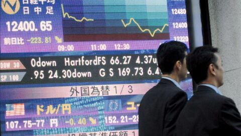 Dos hombres de negocios caminan cerca de un tabl&oacute;n electr&oacute;nico en Tokio