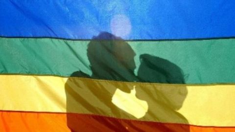 Dos j&oacute;venes se besan tras la bandera LGTB