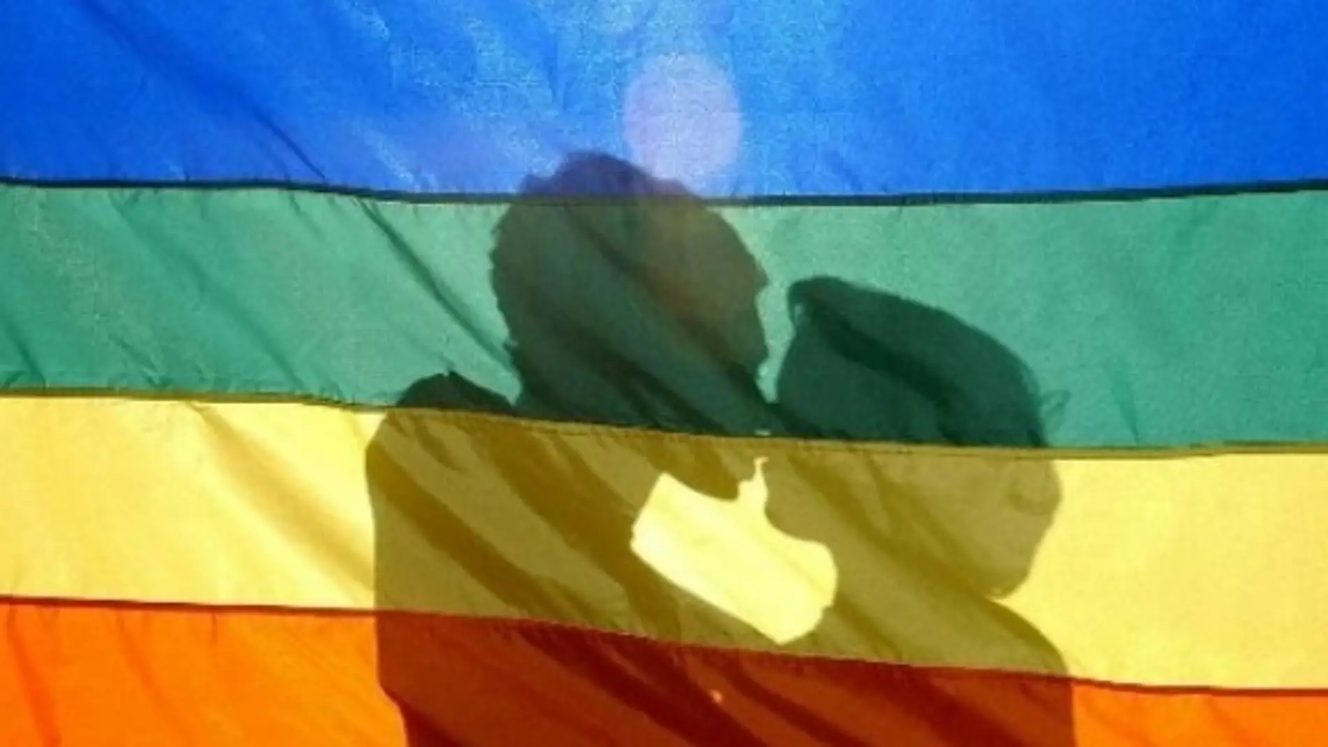 Dos jóvenes se besan tras la bandera LGTB