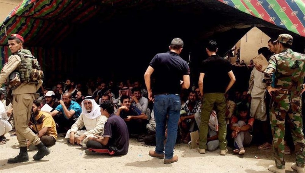 Policías iraquíes vigilan a varias personas que quedaron bajo custodia durante una operación militar en el norte de Faluya