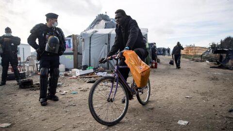 Agentes de polic&iacute;a galos observan a varios migrantes que son evacuados del campamento de Calais