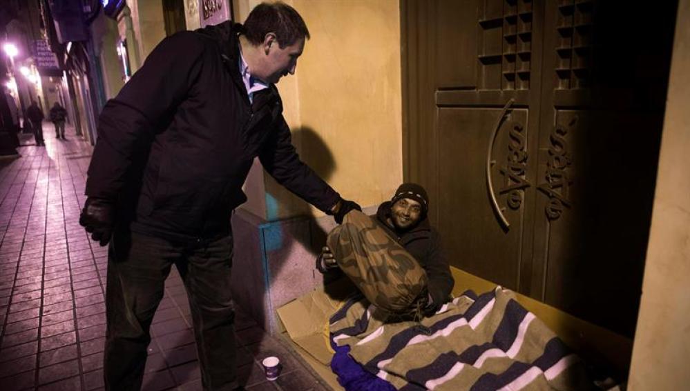 Un policía local entrega un saco de dormir a un 'sintecho' en Valencia