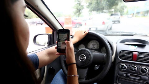 Una mujer mira el m&oacute;vil mientras conduce