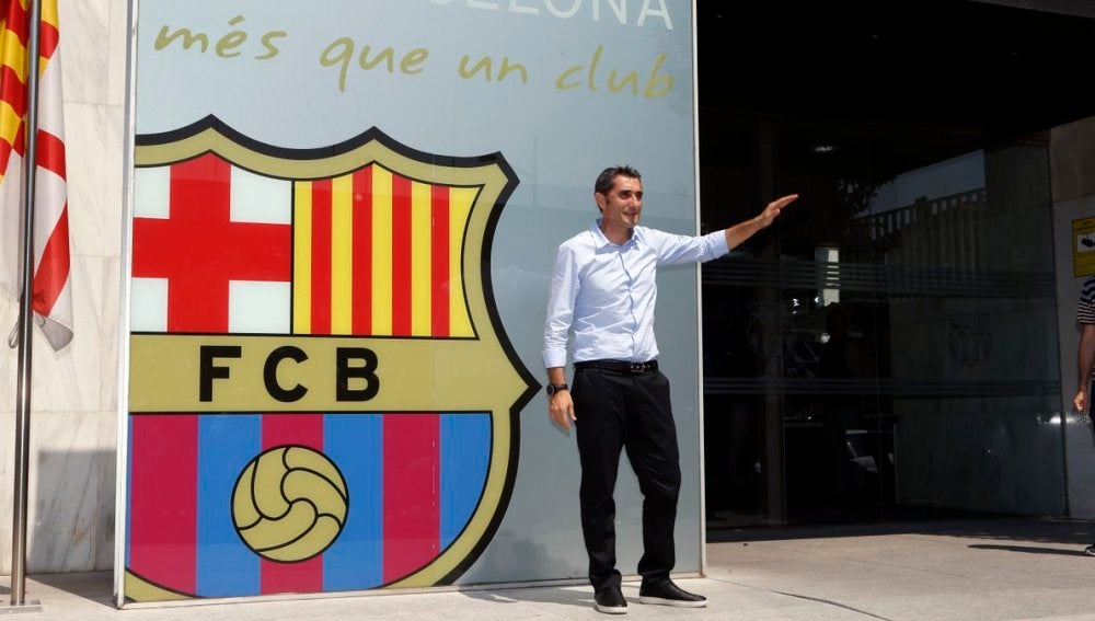 Ernesto Valverde saluda a la prensa mientras posa con el escudo del Barça detrás