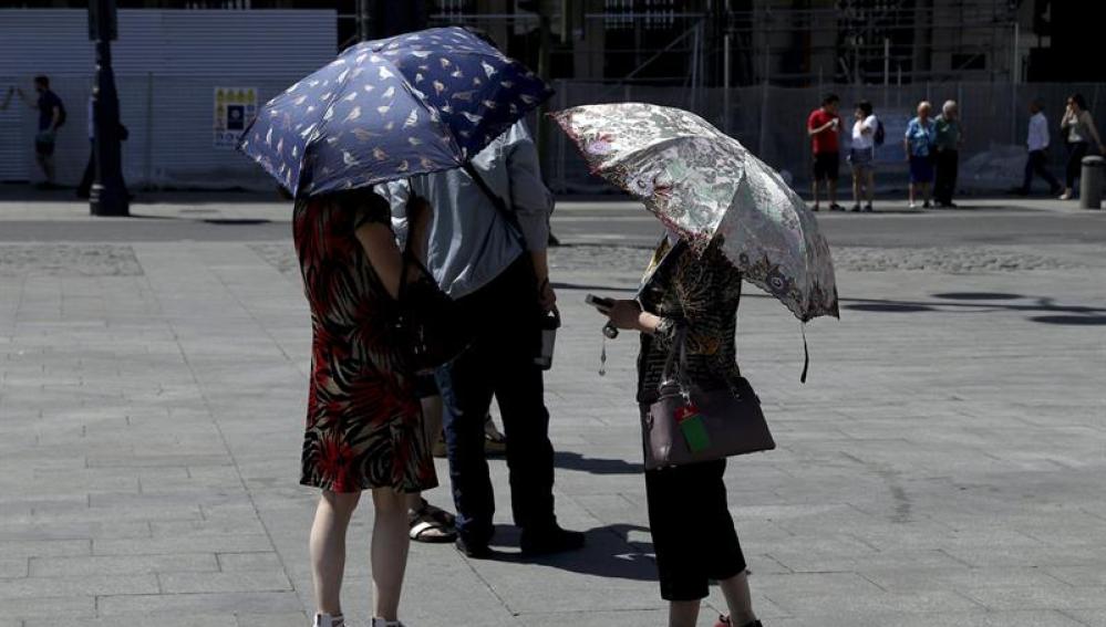 Varias personas se protegen del sol con paraguas en la Puerta del Sol (Madrid)