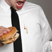 Un hombre se mancha la camisa comiendo una hamburguesa