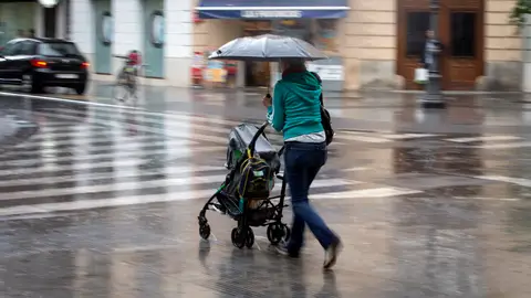 Una mujer con un carrito se protege con un paraguas de la lluvia