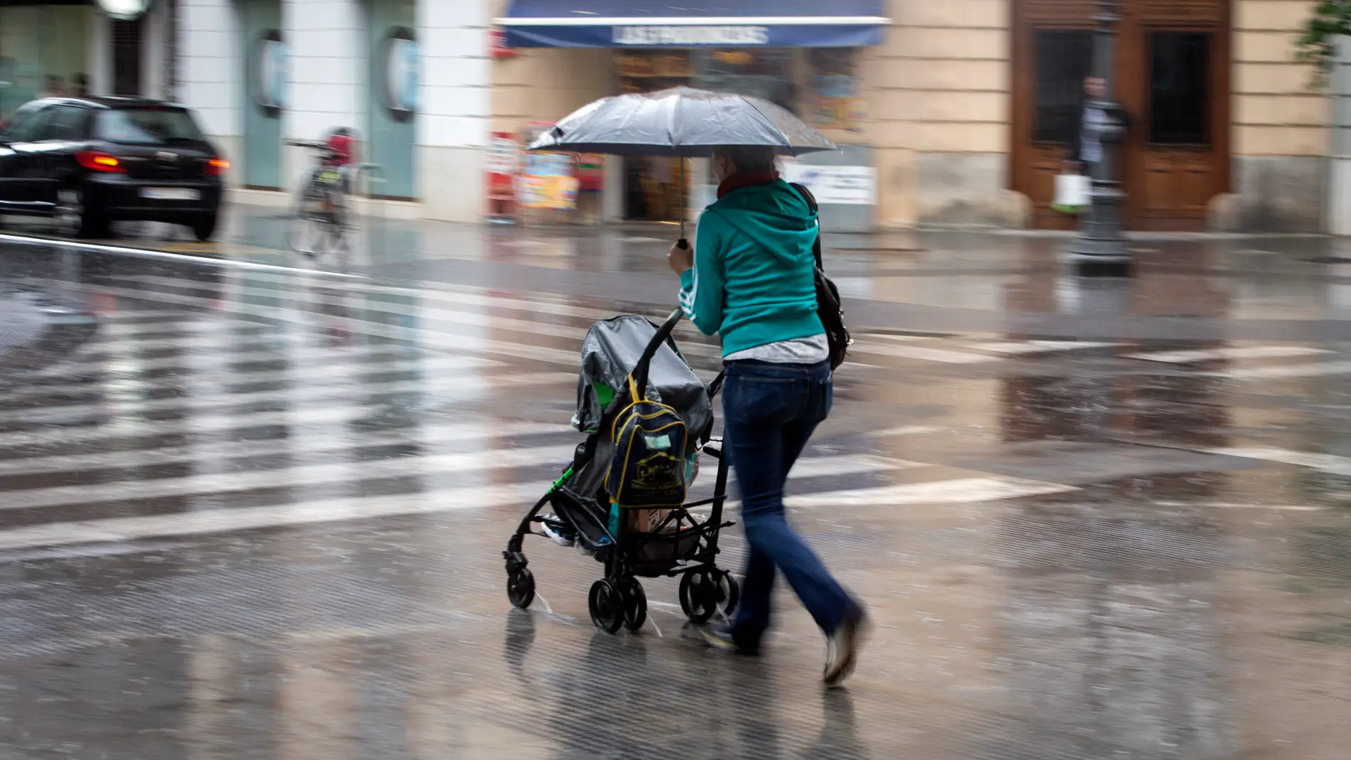 Una mujer con un carrito se protege con un paraguas de la lluvia