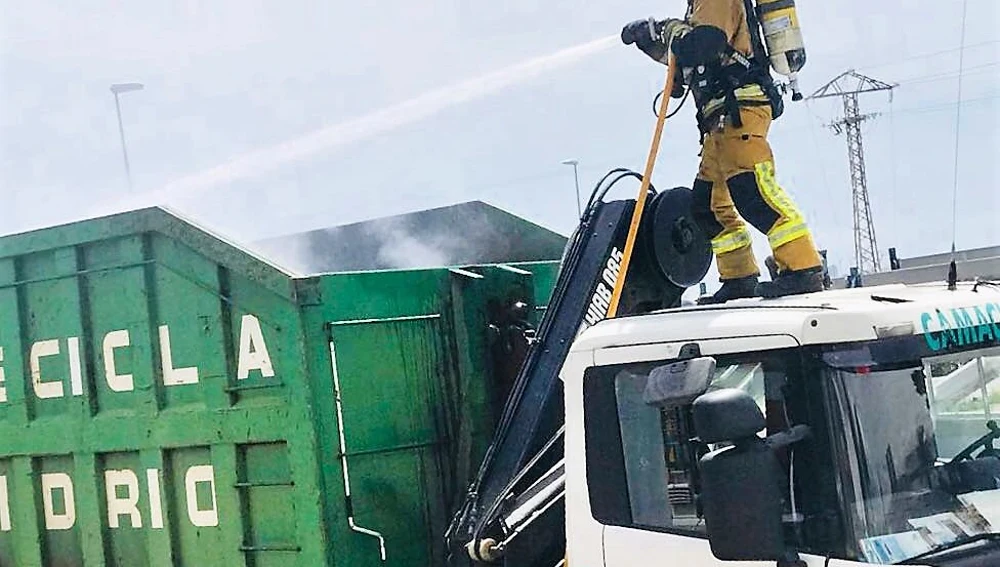 Un bomberos sobre el camión de reciclado incendidado