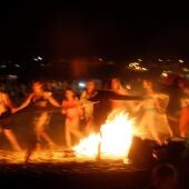 Un grupo de personas baila alrededor de una hoguera en la playa.