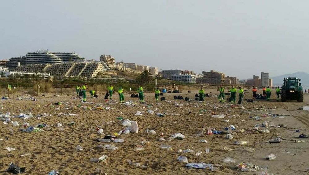 Operarios del servicio de limpieza recogen la basura acumulada en la playa El Carabassí de Elche después de la noche de San Juan.