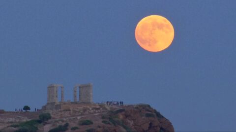 Una luna llena se levanta durante un eclipse lunar detr&aacute;s de la estatua de la antigua diosa Atenea en Atenas