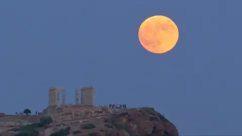 Una luna llena se levanta durante un eclipse lunar detrás de la estatua de la antigua diosa Atenea en Atenas Una luna llena se levanta durante un eclipse lunar detrás de la estatua de la antigua diosa Atenea en Atenas