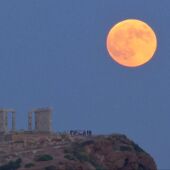 Una luna llena se levanta durante un eclipse lunar detrás de la estatua de la antigua diosa Atenea en Atenas