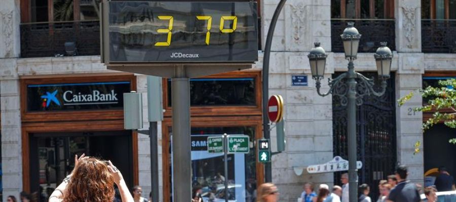 Una mujer toma una fotografía de un termómetro urbano. Una mujer toma una fotografía de un termómetro urbano.