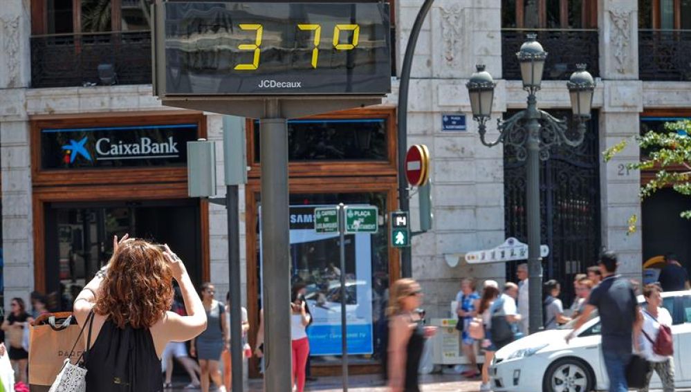 Una mujer toma una fotografía de un termómetro urbano.
