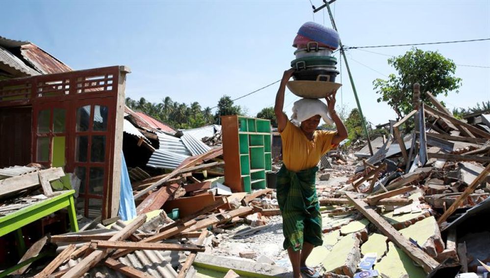 Una mujer carga con sus pertenencias entre los escombros en Lombok (Indonesia) tras el terremoto