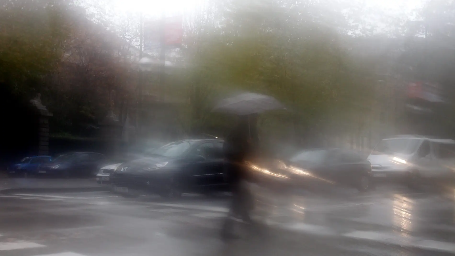 Una persona que cruza un paso de cebra se cubre de la lluvia con un paraguas en un temporal