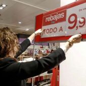 Una empleada de una gran superficies colocando el cartel de 'Rebajas'.