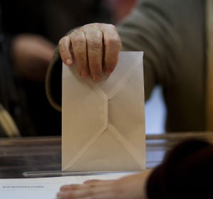 Una persona introduce un sobre en una urna electoral. Una persona introduce un sobre en una urna electoral.