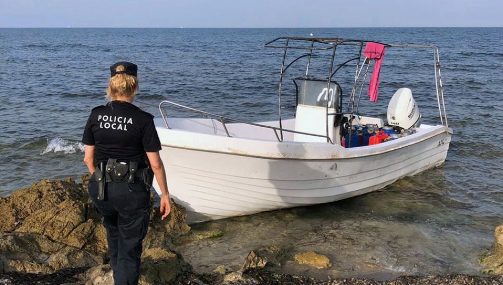 Una agente de la Policía Local de Elche junto a la embarcación con migrantes que ha llegado a la playa del Carabassí.