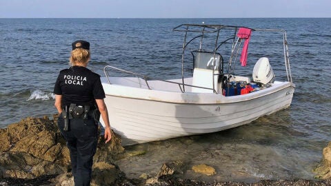 Una agente de la Polic&iacute;a Local de Elche junto a la embarcaci&oacute;n con migrantes que ha llegado a la playa del Carabass&iacute;.