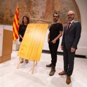 La consellera de Presidencia, Meritxell Budó, y el vicepresidente del Parlament, Josep Costa, acompañados del creador artístico del cartel del acto oficial de la Diada.