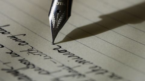 Imagen de archivo de una pluma escribiendo una nota