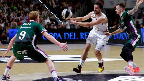 El base Sergio Llull del Real Madrid realiza un pase ante los jugadores del Unicaja M&aacute;laga, el base Alberto D&iacute;az y el base estadounidense Josh Adams.