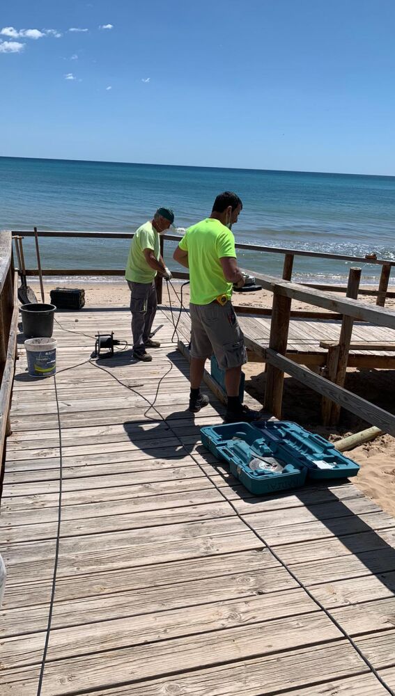Trabajos de reparación de una pasarela en una playa de Elche.