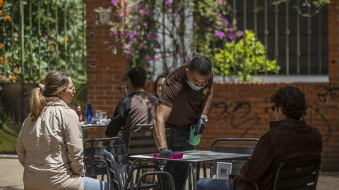 El propietario del bar Arte y Sabor, desinfecta la mesa de un velador a la llegada de unos clientes