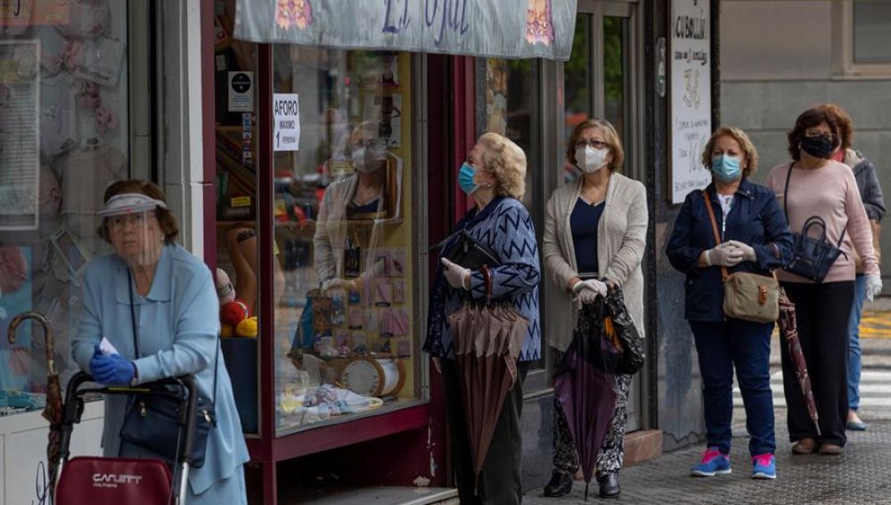 Varias mujeres con mascarillas hacen cola ante una mercería