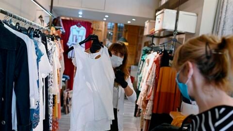 Una trabajadora muestra ropa a una clienta en un comercio de Alcal&aacute; de Henares, Madrid