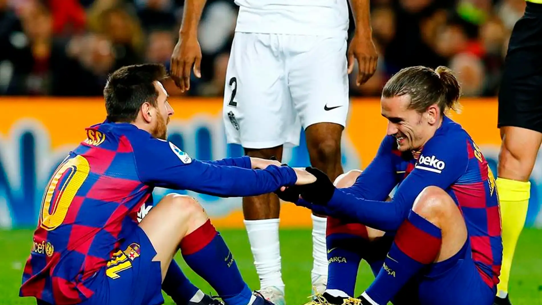 Messi y Griezmann se ayudan a levantarse del césped en un partido con el Barça.