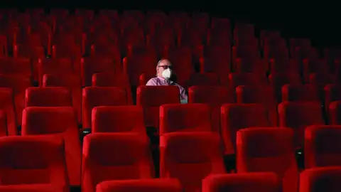 Un espectador espera el comienzo de la película en una sala de cine casi vacía Un espectador espera el comienzo de la película en una sala de cine casi vacía
