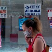 Una mujer con mascarilla pasa ante un comercio cerrado con varios carteles que anuncian su alquiler