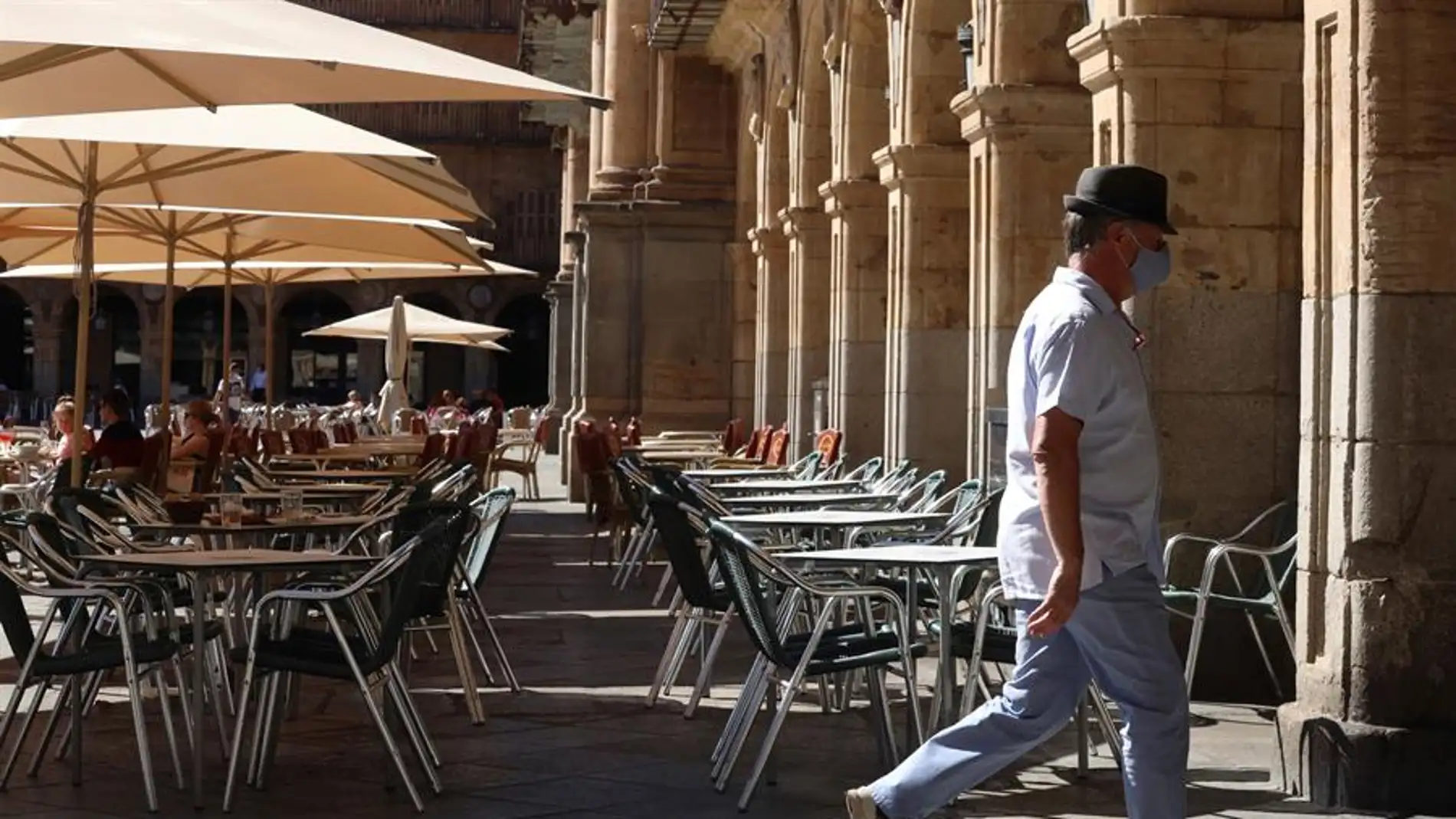 Un hombre con mascarilla pasa frente a una terraza de un restaurante de la plaza mayor de Salamanca.