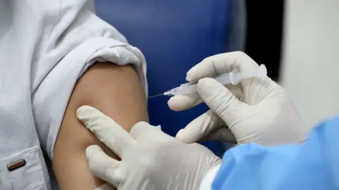 Un sanitario administra una vacuna a un paciente Un sanitario administra una vacuna a un paciente