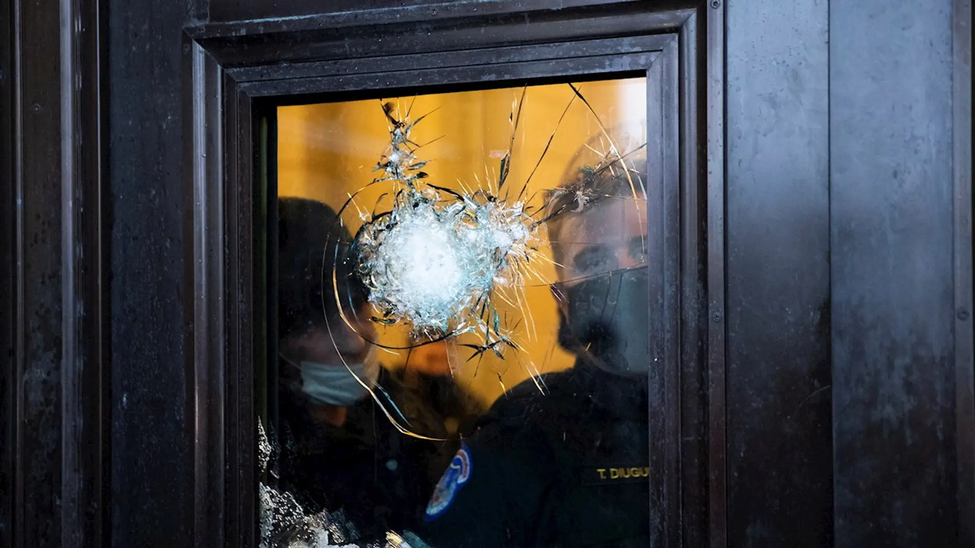 Dos policías observan a través del vidrio roto de una de las puertas del Capitolio de EEUU.