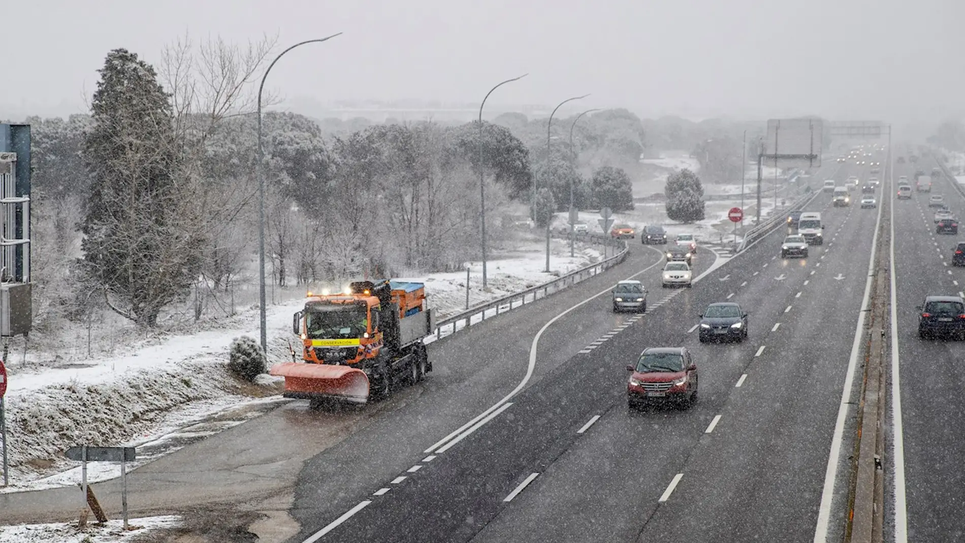 Un quitanieves trabaja mientras varios vehículos circulan por la A-5 a la entrada de Madrid durante el temporal de nieve